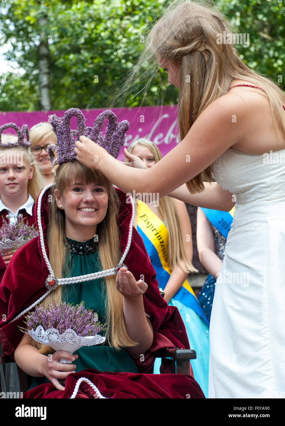 Amelinghausen, Germany. 23rd Aug, 2015. 22-year-old Victoria Glaser (L) is crowned by her predecessor Sophia Wischmann (R) after being elected the new Heather Queen in Amelinghausen, Germany, 23 August 2015. The annual Heather Blossom Festival culminates in the election of the Heather Queen. After the coronation, a precession featuring festively decorated floats, music bands and other groups is held in the town. The new Heather Queen will now represent the region across Germany for a year. PHoto: PHILIPP SCHULZE/dpa/Alamy Live News Stock Photo