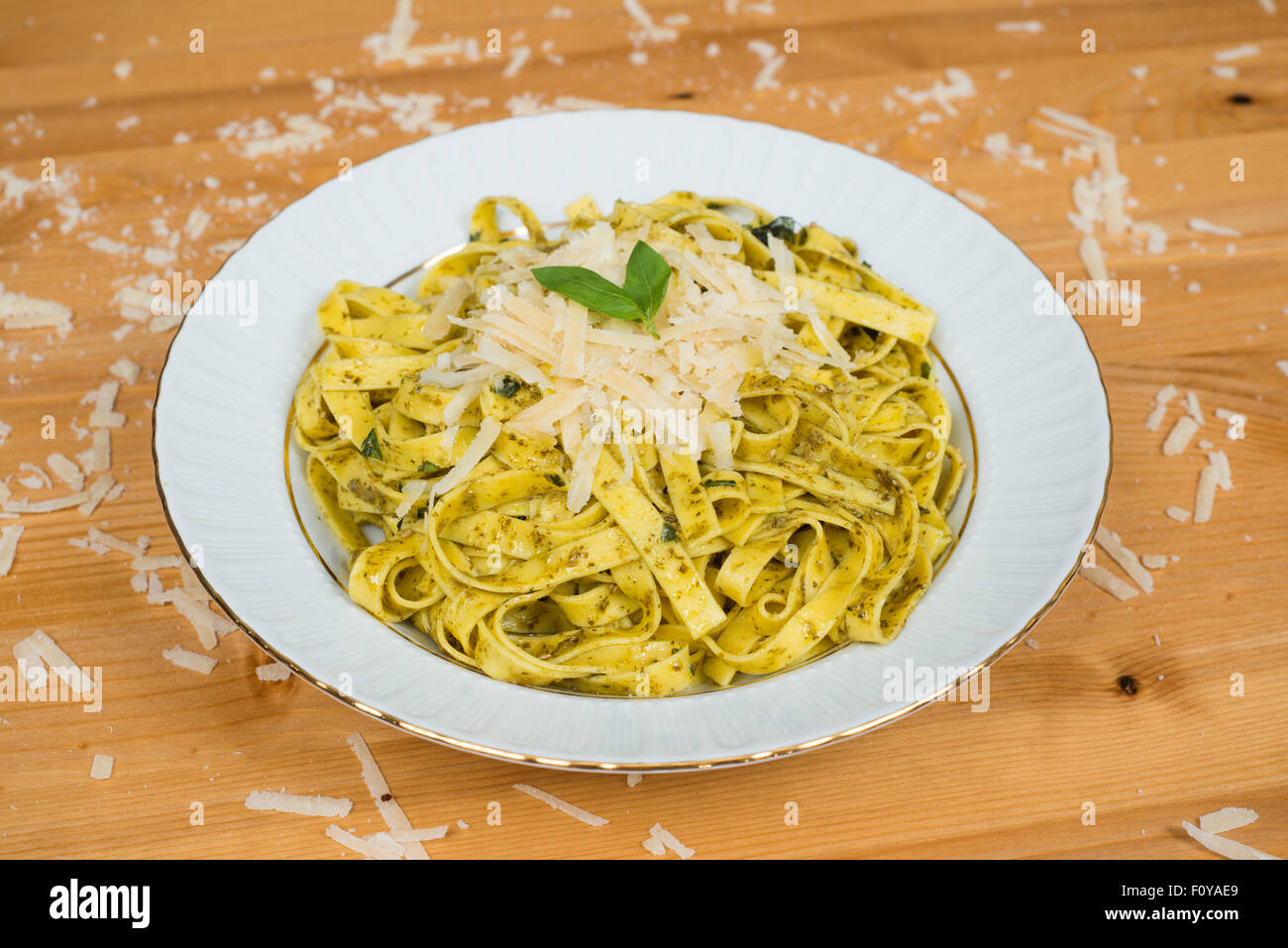 Tagliatelle pasta with pesto sauce and basil leafs on white plate, wood background Stock Photo