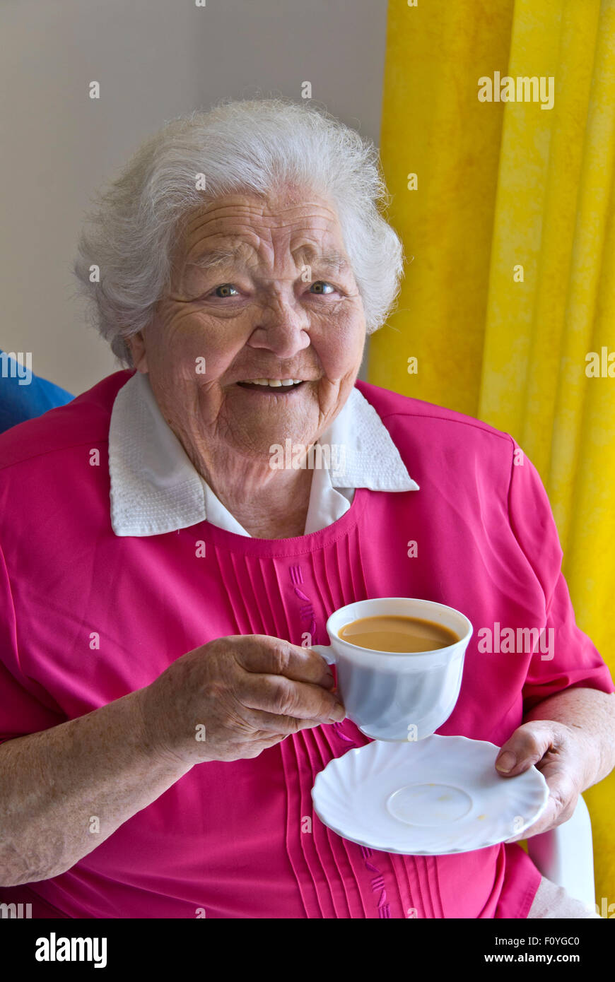 Happy content senior elderly lady sitting at home in her light airy room with a cup of tea Stock Photo