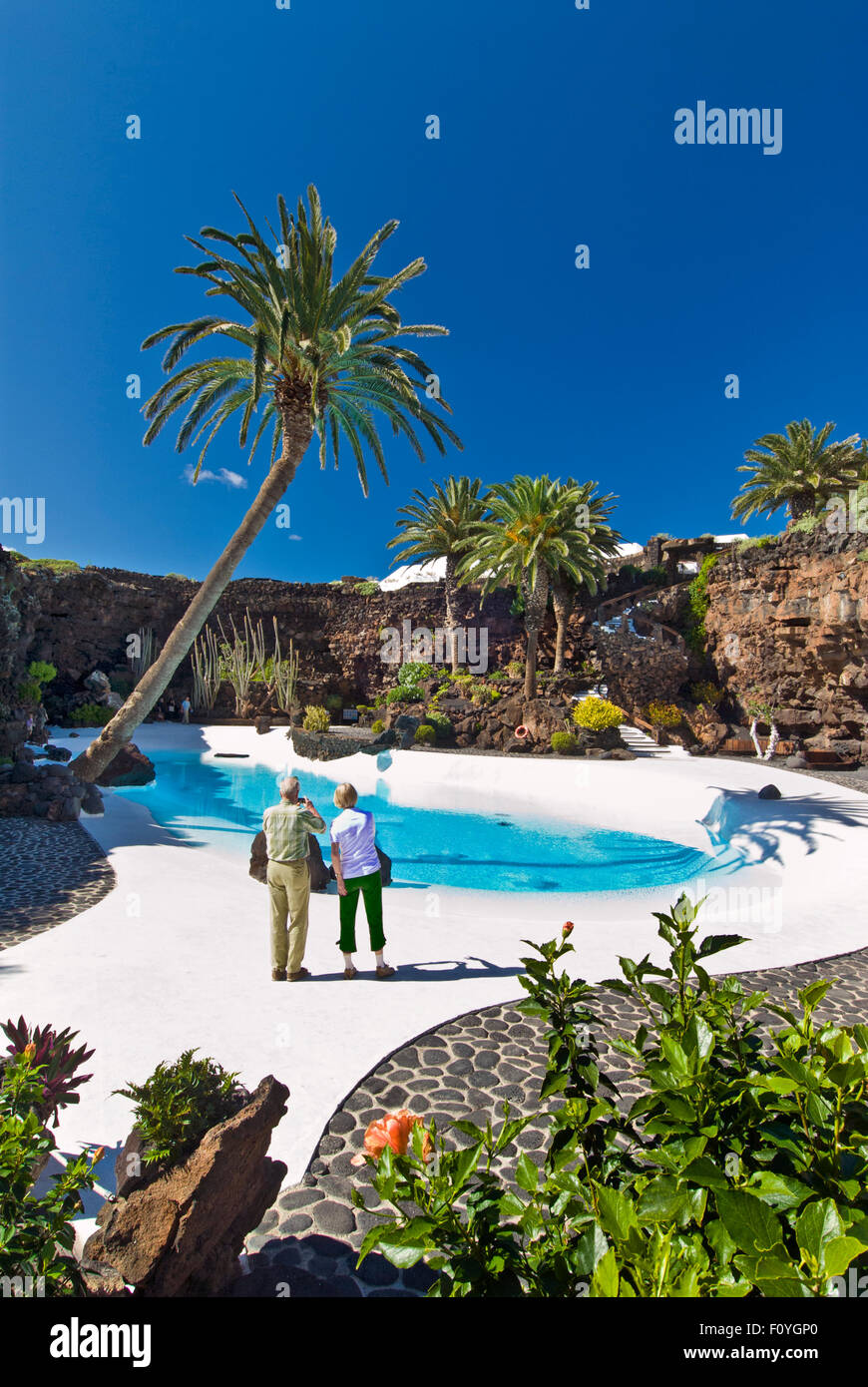 LANZAROTE Jameos del Agua Tourist couple taking photo of clear turquoise pool with palms and tropical plants, Manrique, Lanzarote Canary Islands Spain Stock Photo