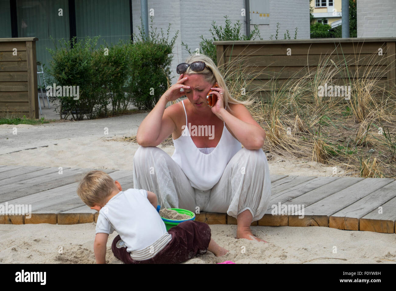 A parent talking on cell phone while she plays with her son Stock Photo