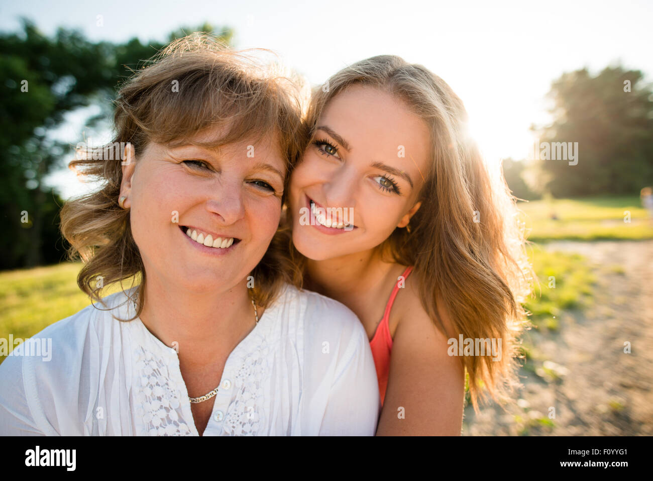 Portrait of mother and her teenage daughter outdoor in nature with setting sun in background Stock Photo