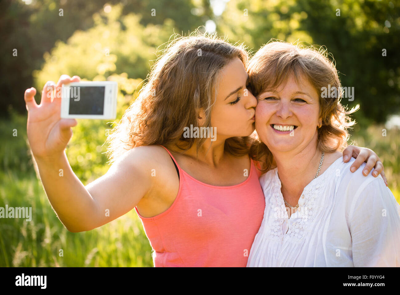 Adult daughter kissing her senior mother while taking selfie photo with mobile phone Stock Photo