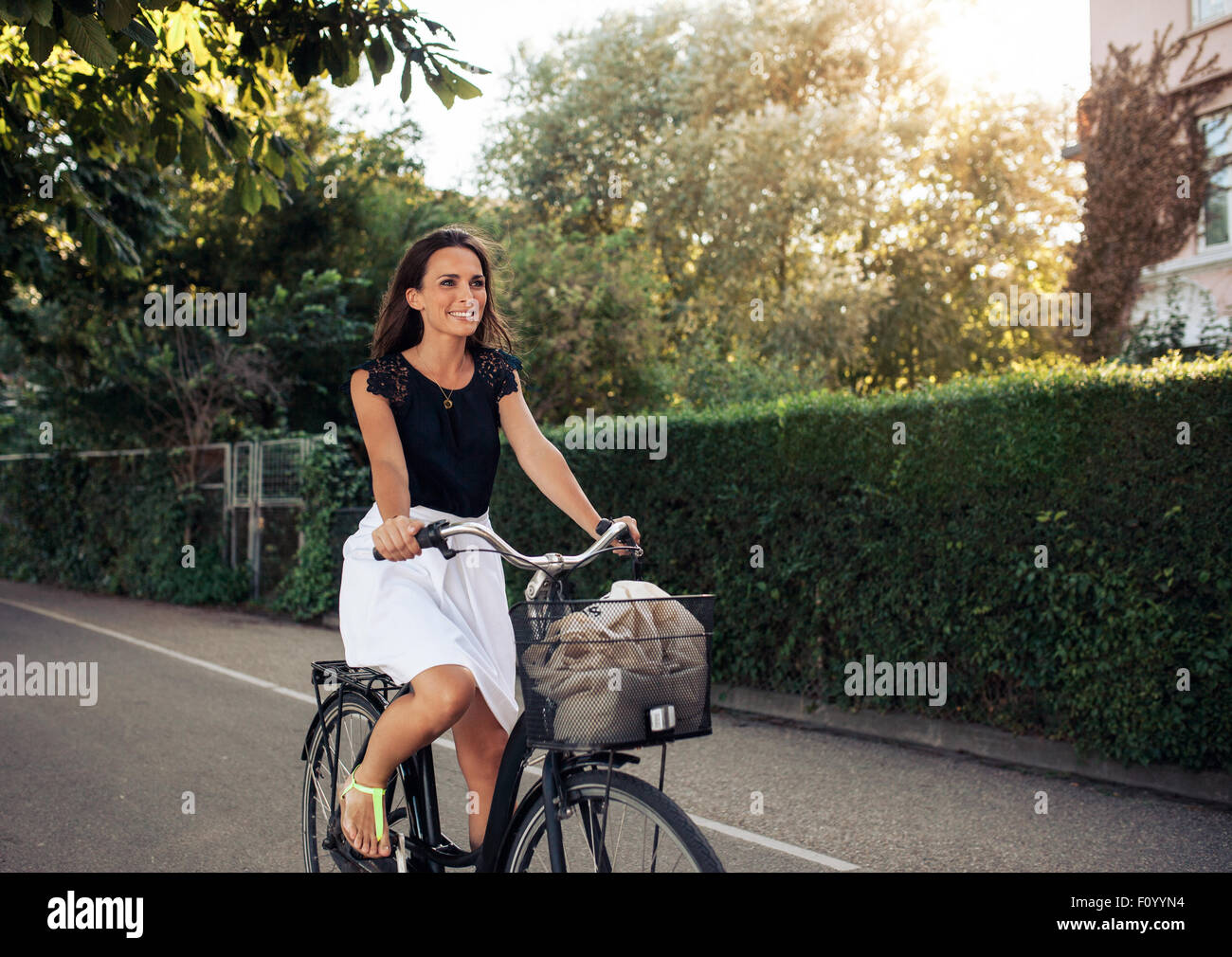 Portrait of a beautiful young woman cycling along street. Smiling woman riding her bicycle on city street. Stock Photo