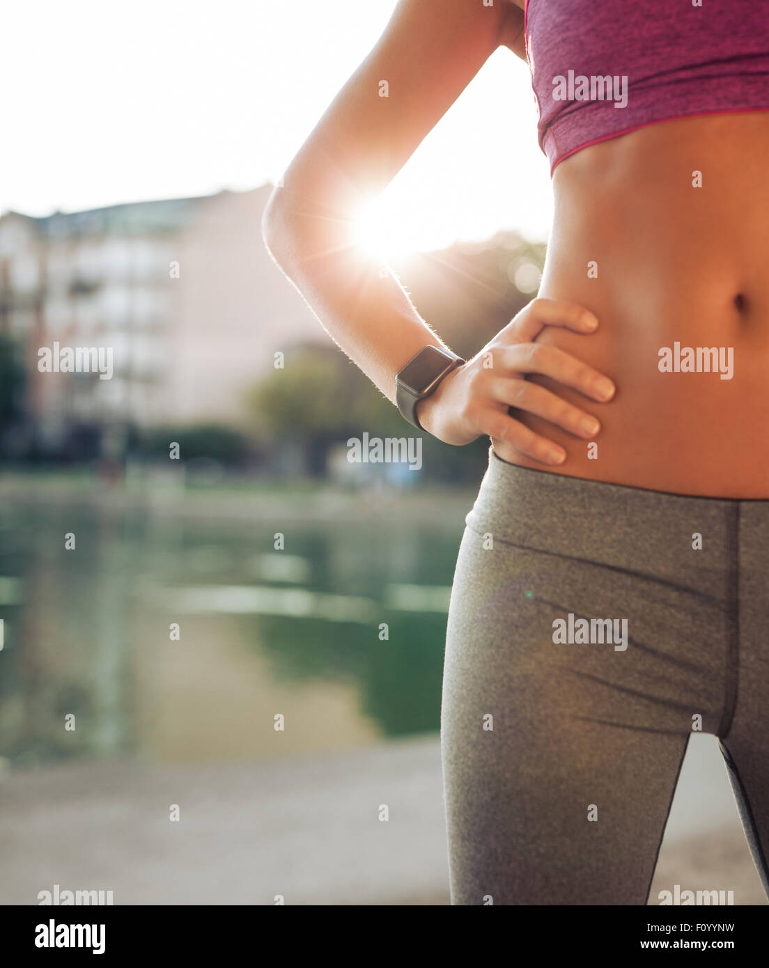 Cropped shot of fitness model wearing smartwatch standing with her hands on hips on a summer day. Female runner relaxing after s Stock Photo