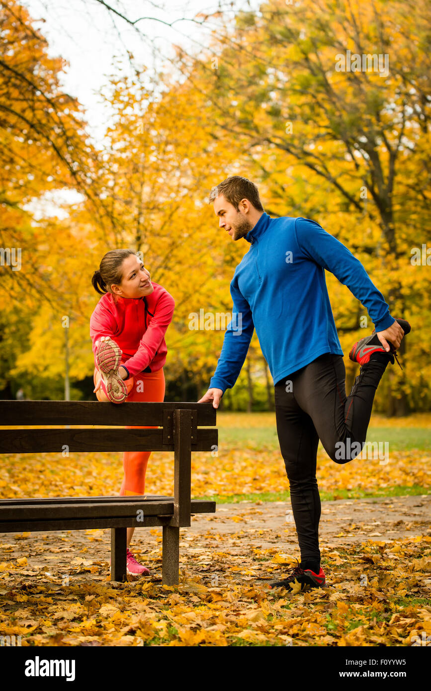Young couple stretching muscles on bench before jogging in autumn nature Stock Photo