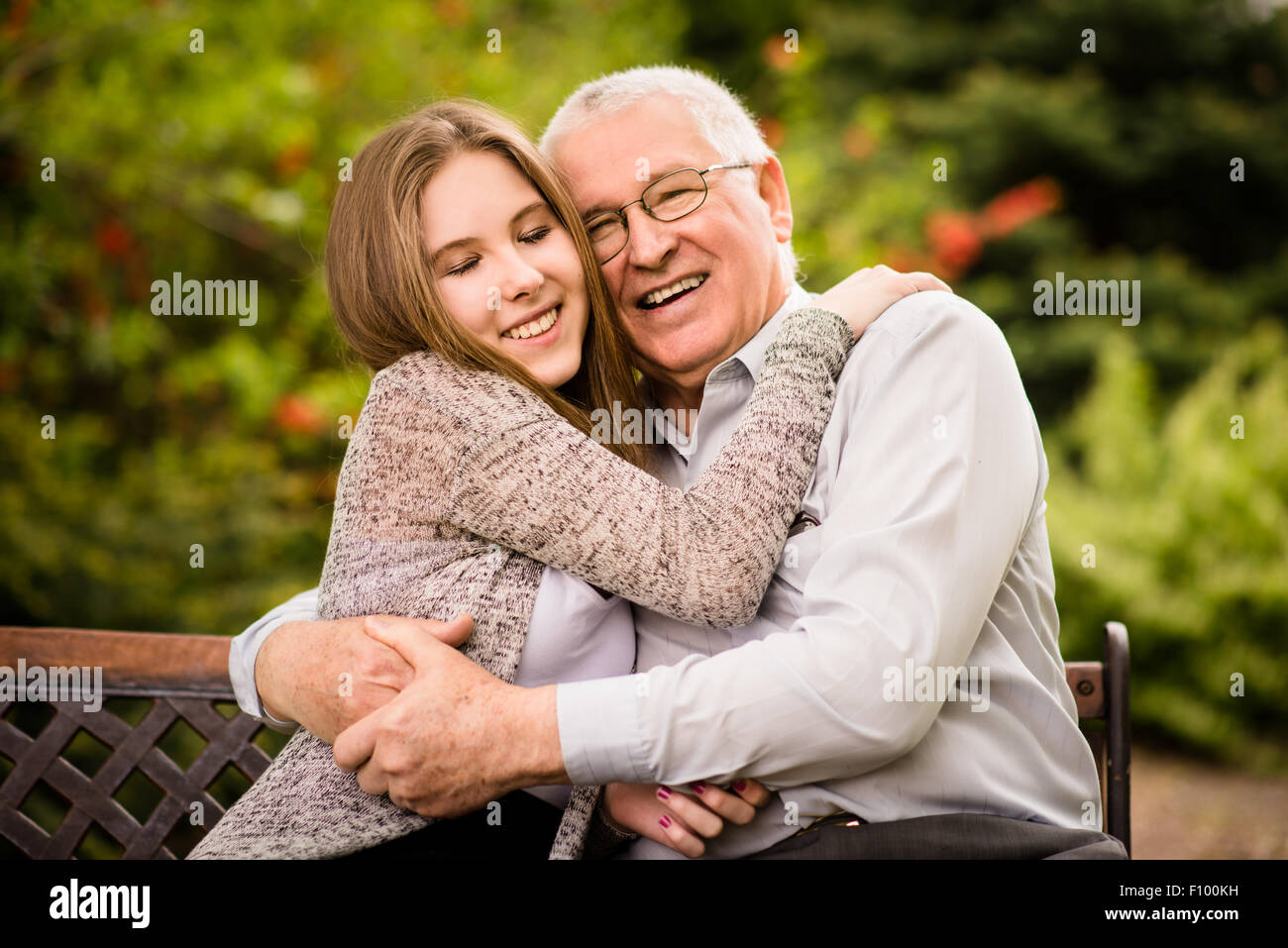Authentic photo of smiling grandfather hugging with his teenage granddaughter outdoor in nature Stock Photo