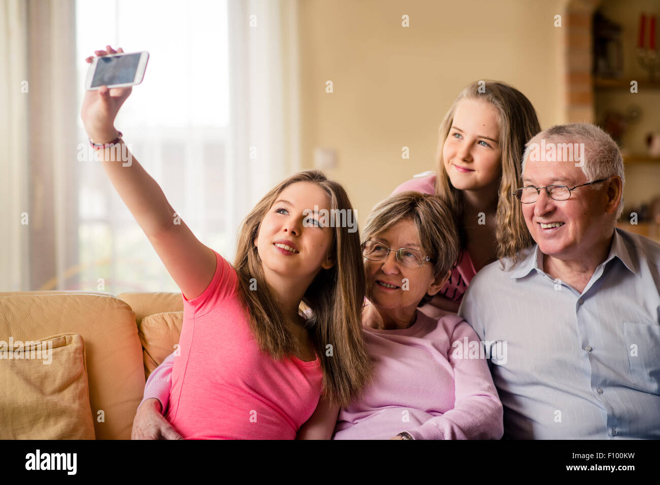 Teenage girl taking photo with mobile phone of herself, sister and her grandparents at home on sofa Stock Photo