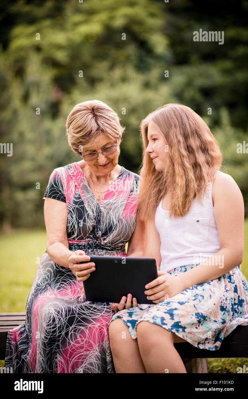 Senior woman with her granddaughter looking together on photos in smartphone - outdoor in nature Stock Photo