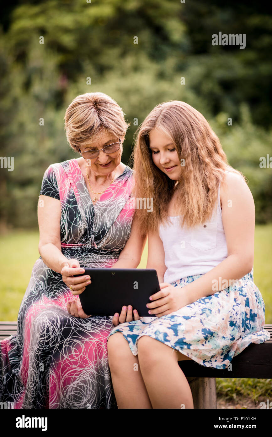 Senior woman with her granddaughter looking together on photos in smartphone - outdoor in nature Stock Photo