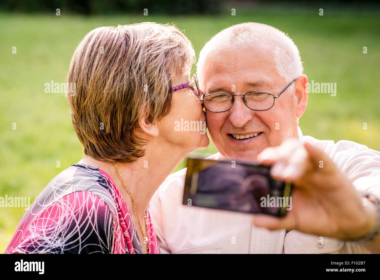 Happy senior couple taking picture of themselves by smartphone - woman is kissing man Stock Photo