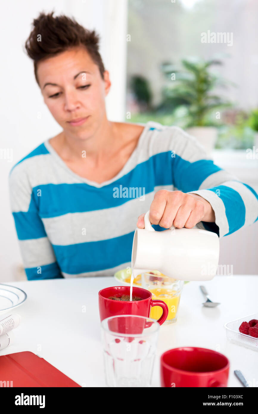 Woman pouring milk in her morning coffee at the breakfast table. Stock Photo