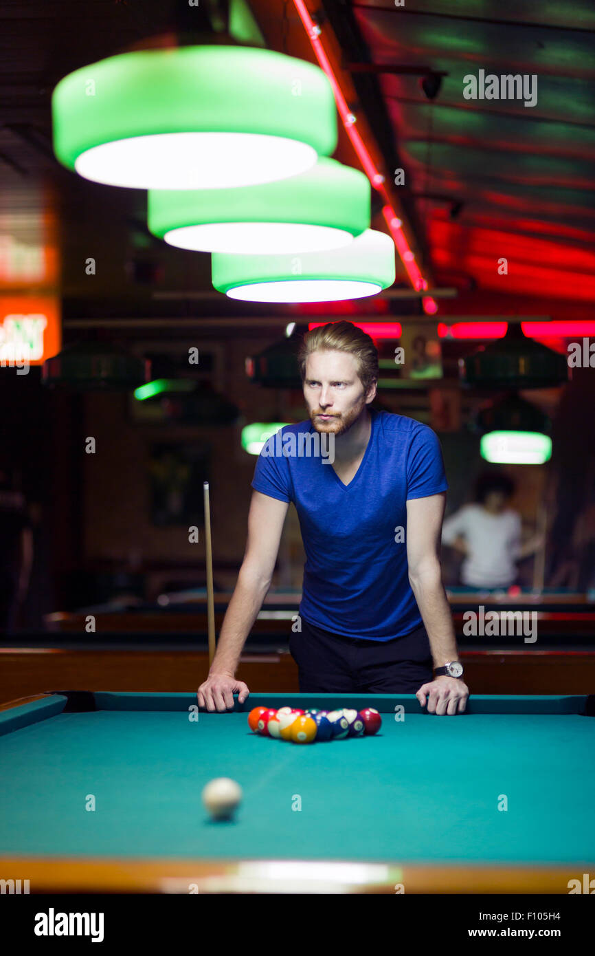 Handsome young snooker player bending over the table in a bar with beautiful ambient lighting Stock Photo