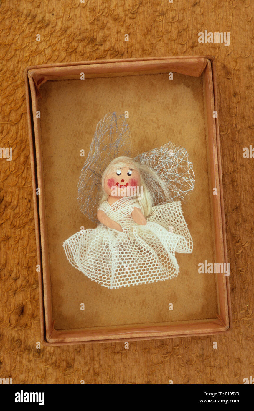 Small fabric model of angel or fairy with smiling face white net dress and crumpled wings lying in cardboard tray Stock Photo