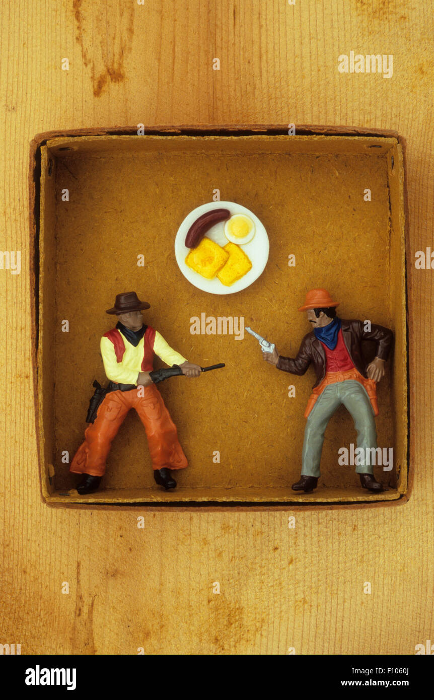 Plastic model of cowboys with rifle and gun drawn fighting over breakfast plate of sausage and egg Stock Photo