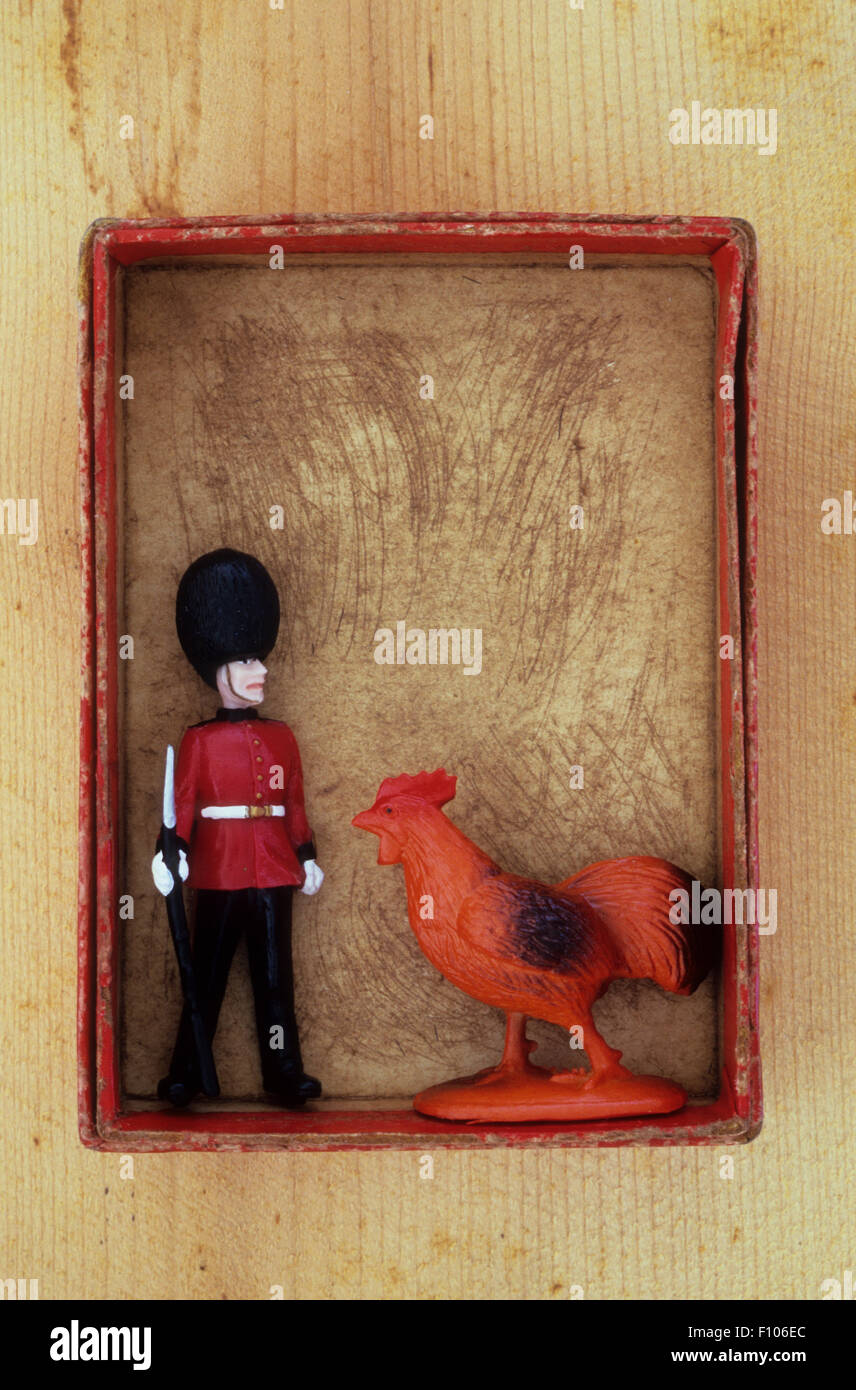 Plastic model of soldier in red jacket and busby standing with rifle on ground and being approached by giant chicken Stock Photo