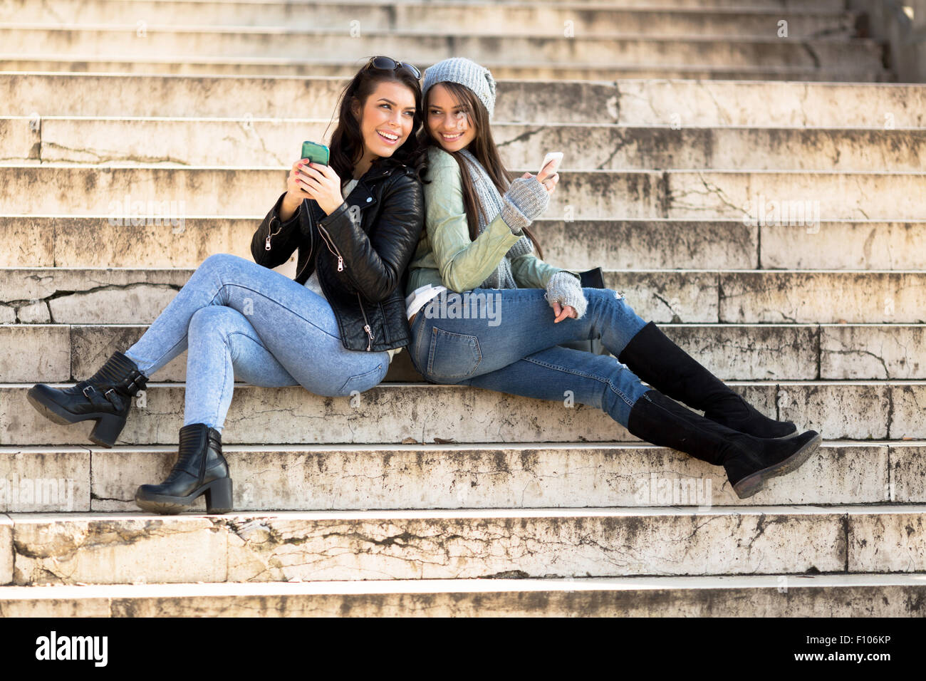 Two young women leaning against each other on stairs and holding cell phones Stock Photo