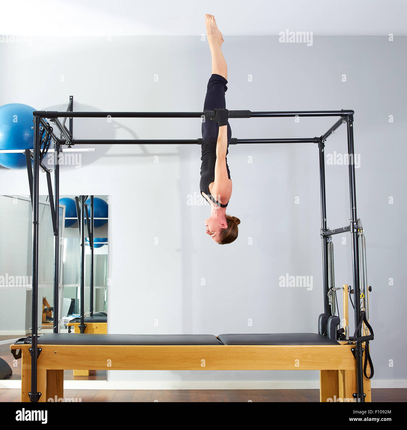 Pilates woman in cadillac acrobatic upside down balance reformer