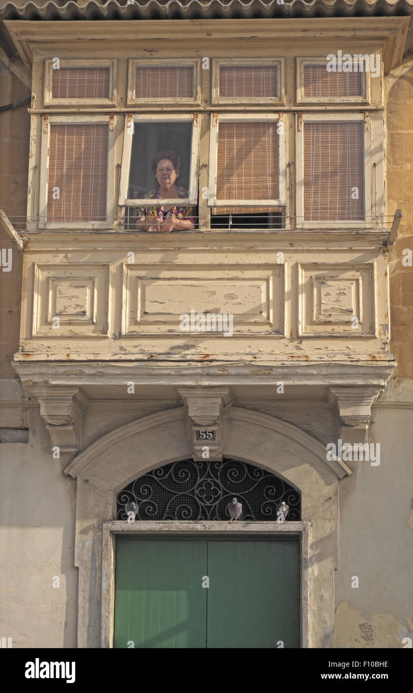 Woman at a window of a wooden balcony with entrance beneath, Valletta waterfront, Malta. Stock Photo