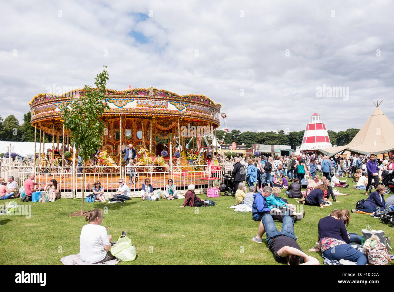Visitors sitting in sunshine resting on lawns by Carousel at RHS Cheshire Flower Show, Tatton Park Knutsford Cheshire England UK Stock Photo