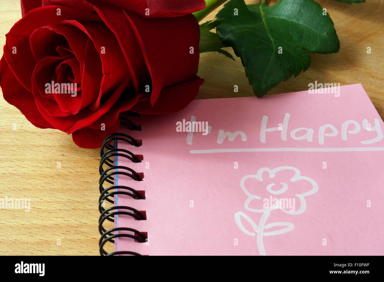 Pink notepad with I am happy and rose on a wooden background. Stock Photo