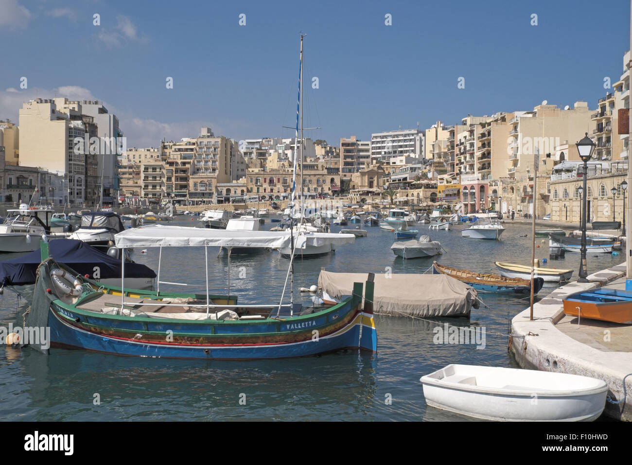 Brightly painted traditional fishing boats with stone buildings beyond, St Julian's Bay, Malta. Stock Photo