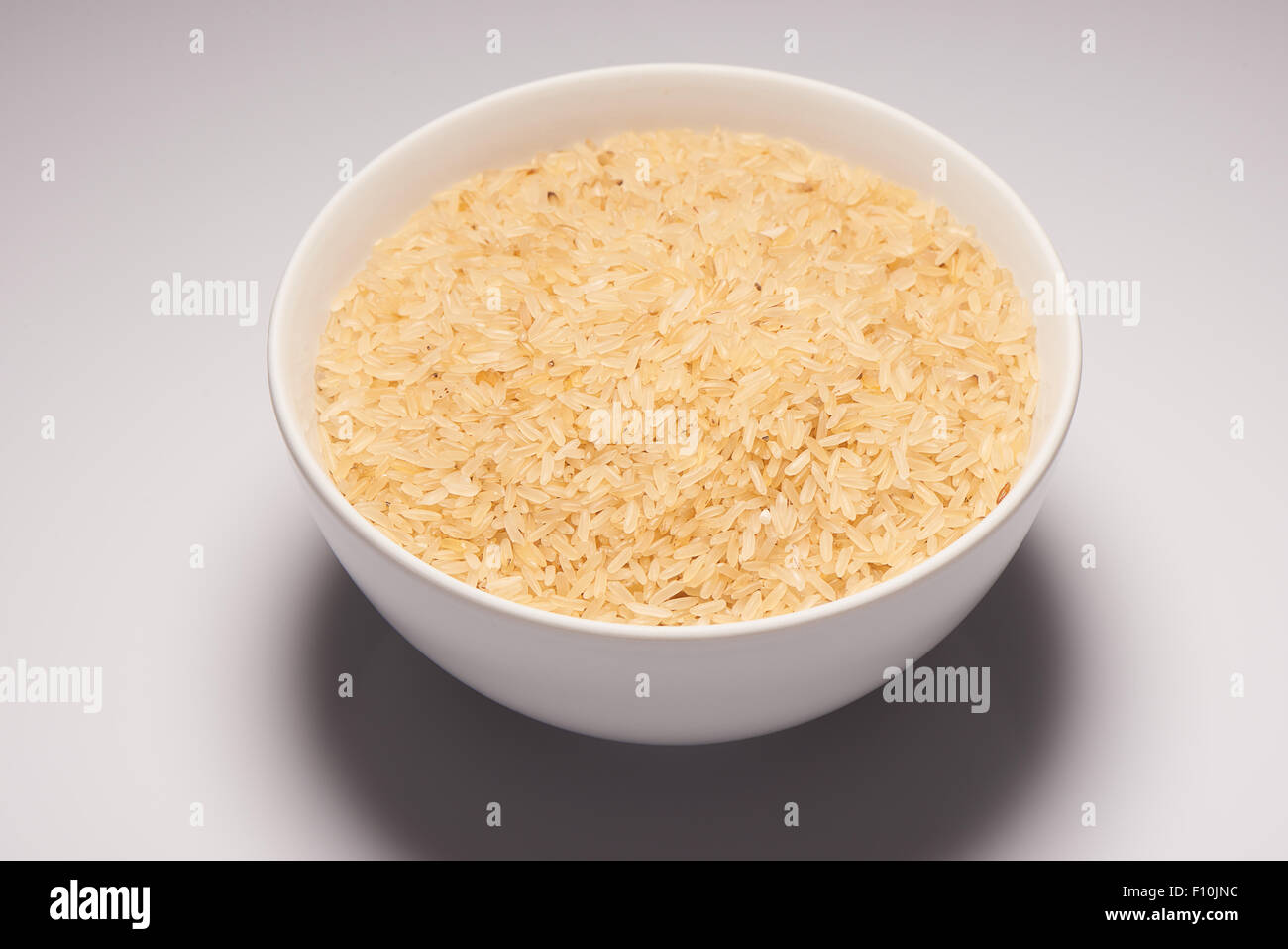 Brown rice seeds in white ceramic bowl on white background Stock Photo