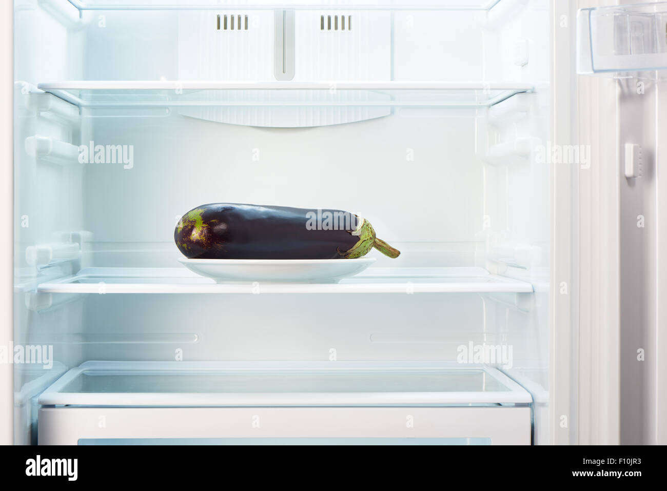 Purple eggplant on white plate in open empty refrigerator. Weight loss diet concept Stock Photo