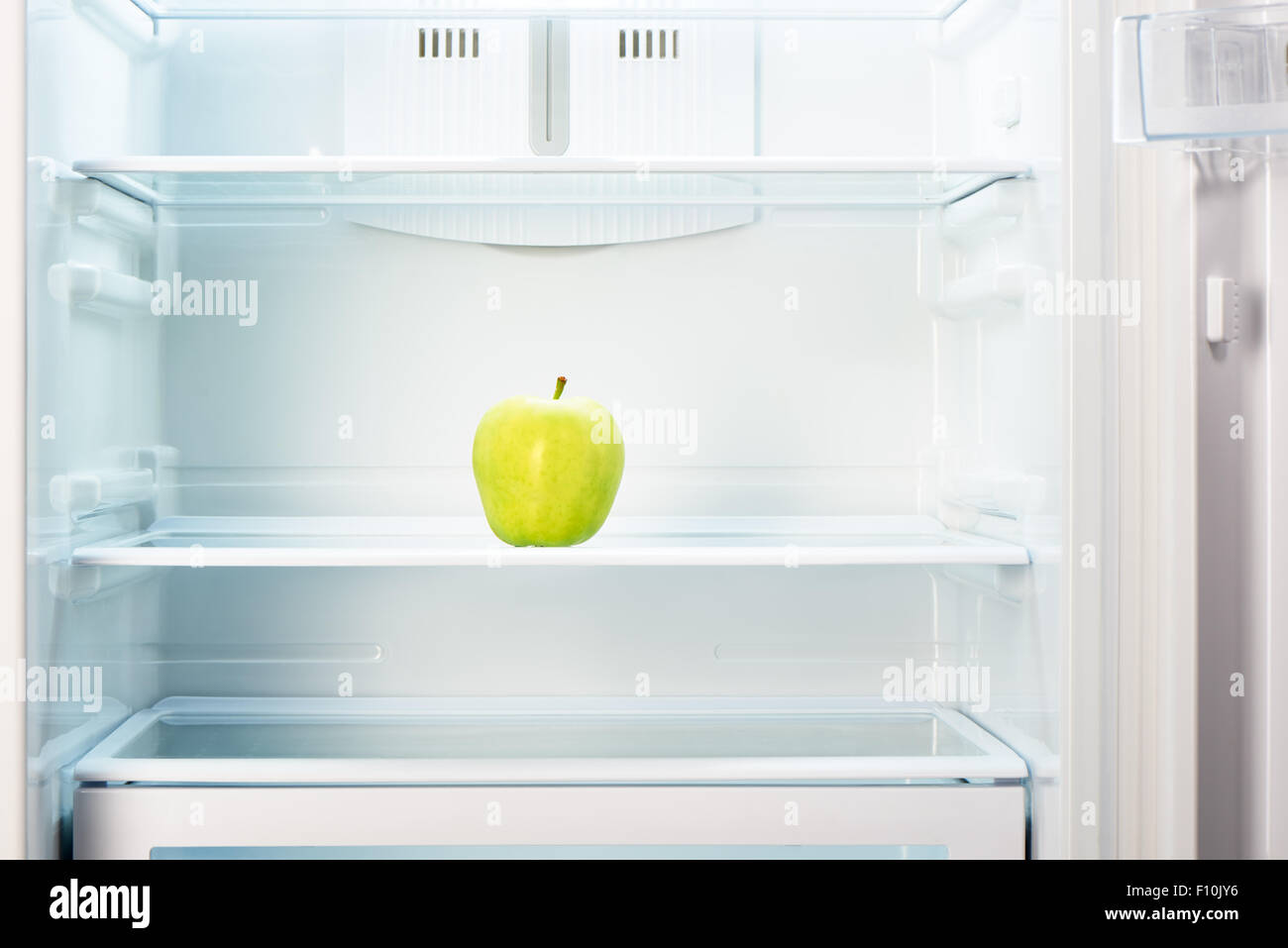Green apple on shelf of open empty refrigerator. Weight loss diet