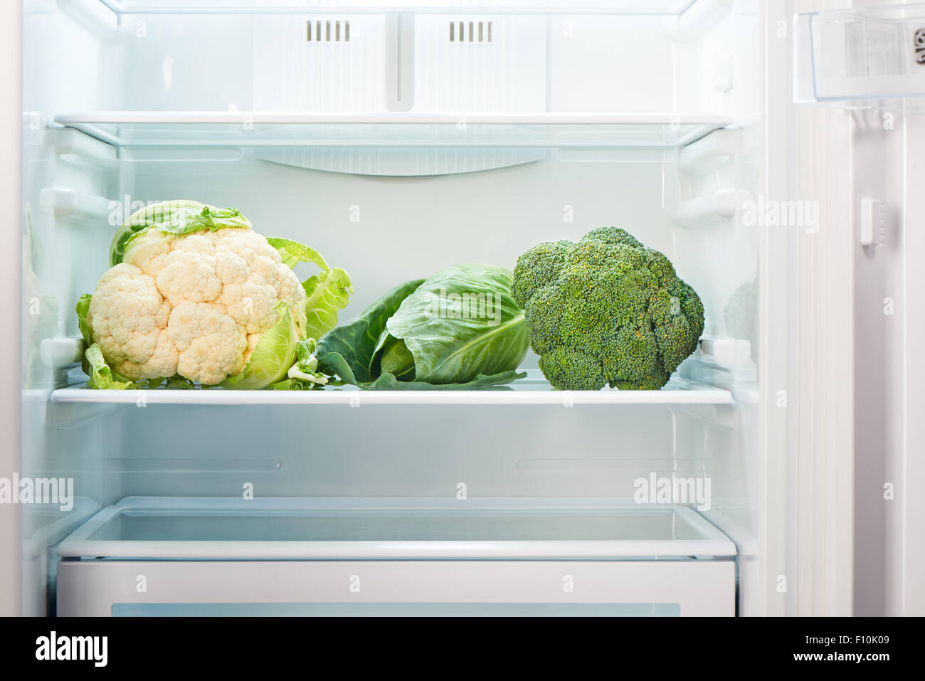 Cauliflower, green cabbage and green broccoli on shelf of open empty refrigerator. Weight loss