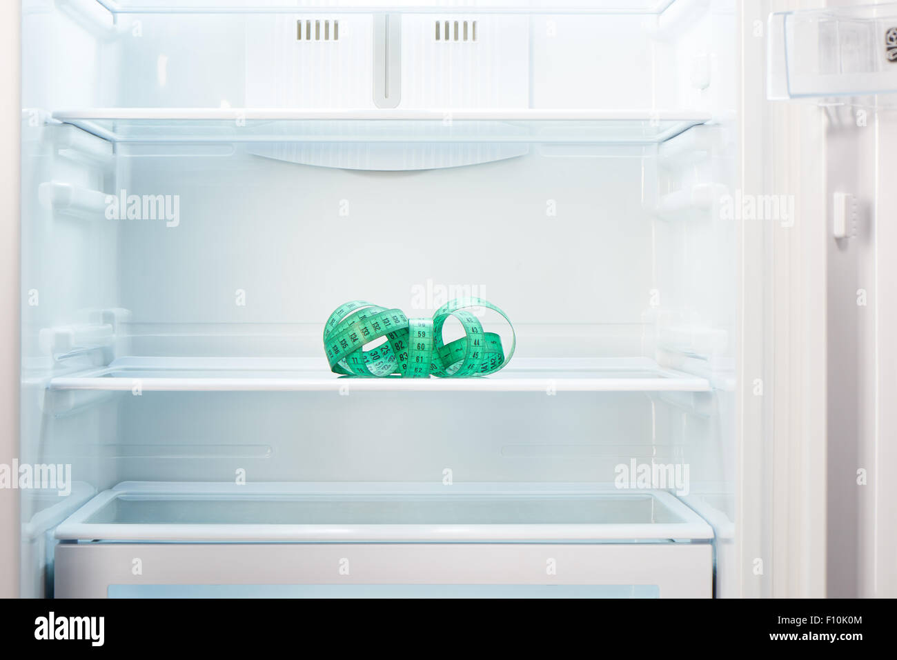 Green measuring tape on shelf of open empty refrigerator. Weight loss diet concept. Stock Photo