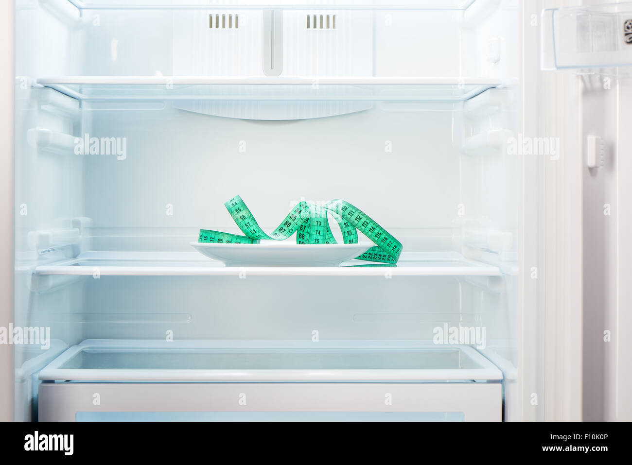 Green measuring tape on white plate in open empty refrigerator. Weight loss diet concept. Stock Photo