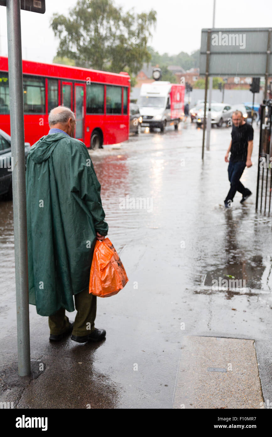 Purley, London, UK, 24th August 2015. An elderly man in a green poncho contemplates the flooded high street. A yellow flood warning for London has been issued by the Met Office. A fortnight's rain is predicted to fall in 24 hours. Credit:  Dave Stevenson/Alamy Live News Stock Photo