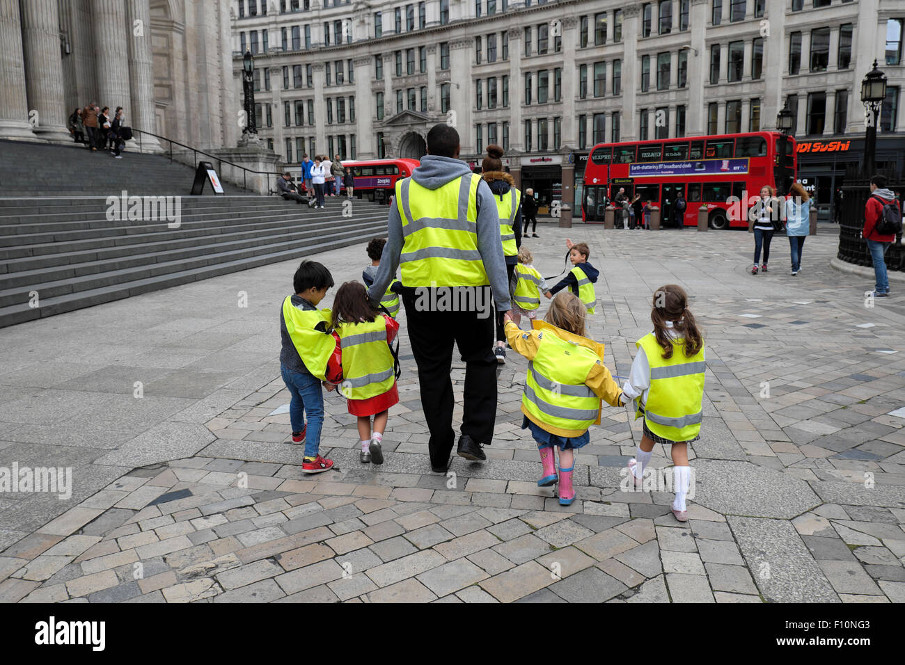 Nursery school children & childminder after crossing road city street back rear view walking outside past St Pauls Cathedral London UK  KATHY DEWITT Stock Photo