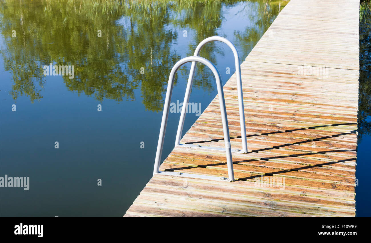 Metal ladder into the pool or lake on a wooden walk way Stock Photo