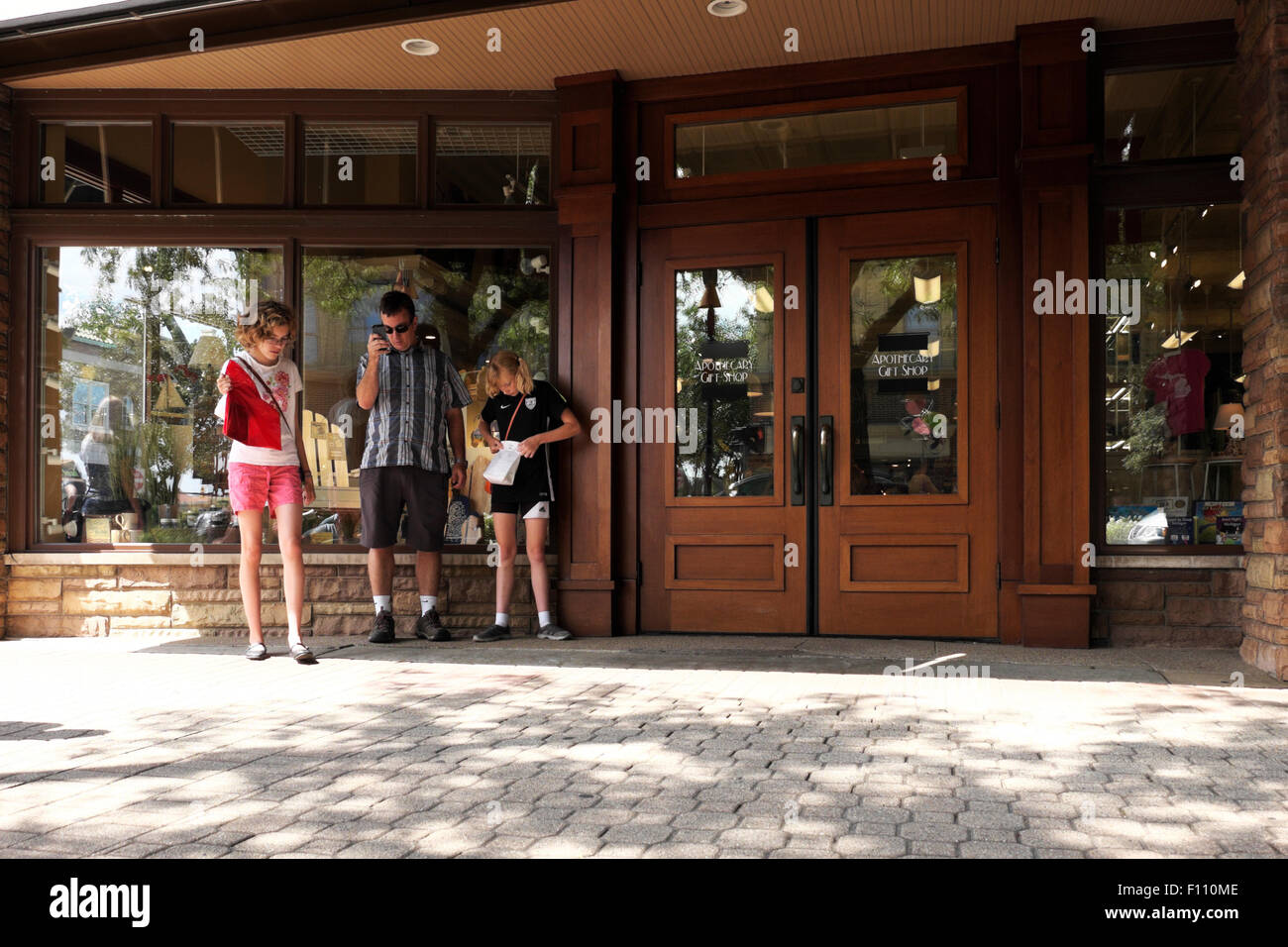 Father, accompanied by his daughters, checks his cell phone outside the Apothecary Gift Shop in downtown Holland, Michigan, USA. Stock Photo