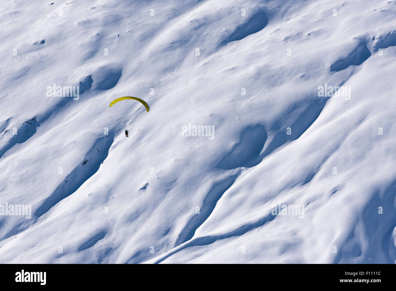 A paraglider is flying high up in the snow covered mountains above a snowfield at Belalp/Blatten, Switzerland (Valais canton). Stock Photo