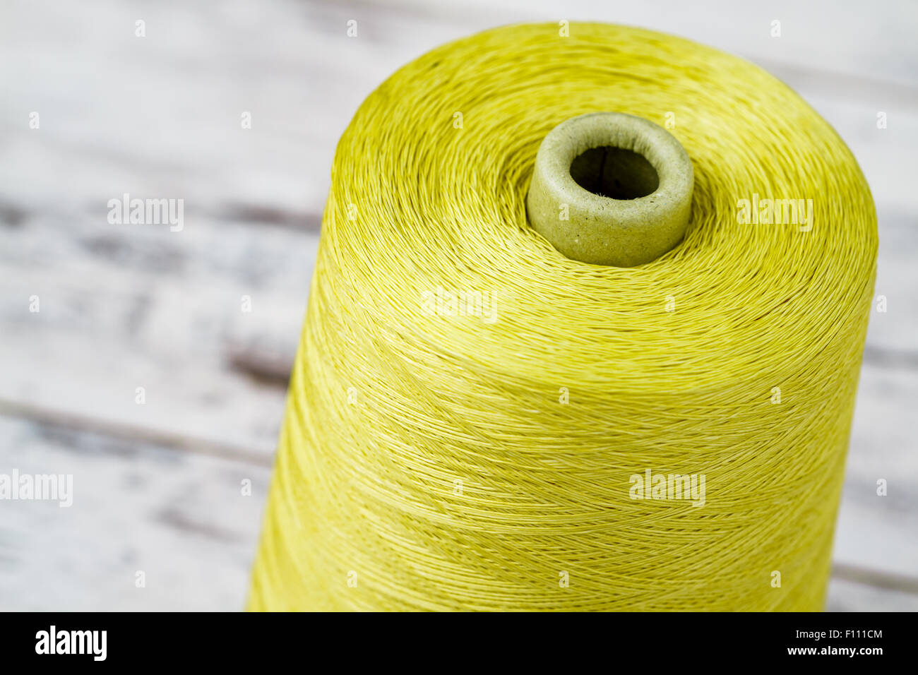 Spool of synthetic green thread on white wooden background Stock Photo