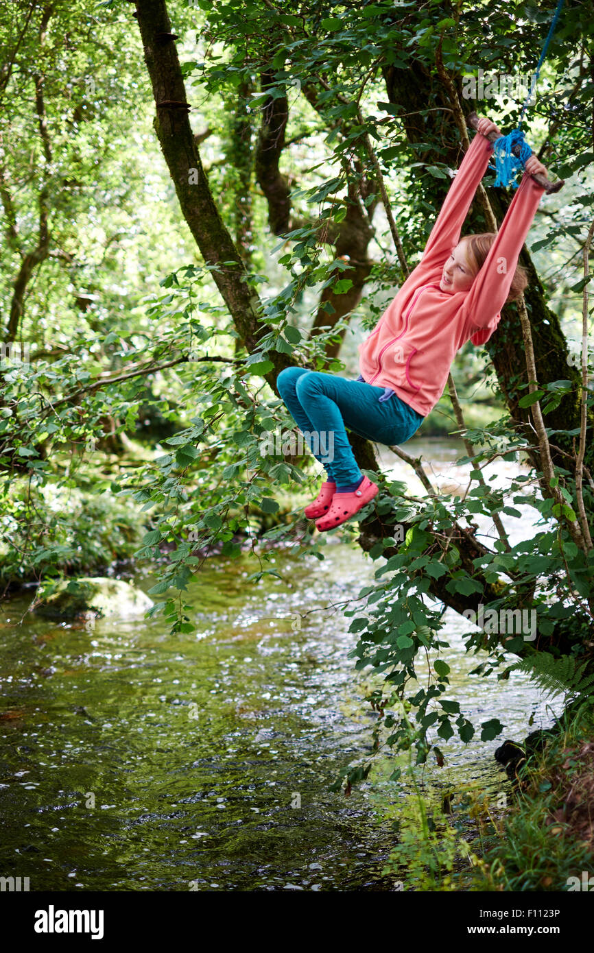 Adventurous girl playing on a rope swing in woodland by the river Dart