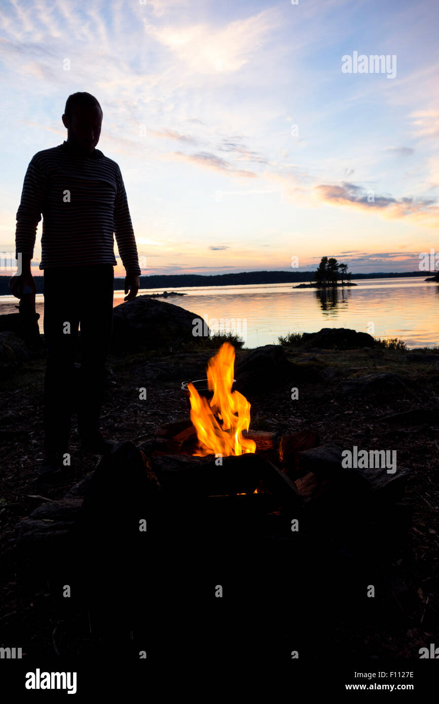 Man standing in front of campfire at dusk Stock Photo - Alamy