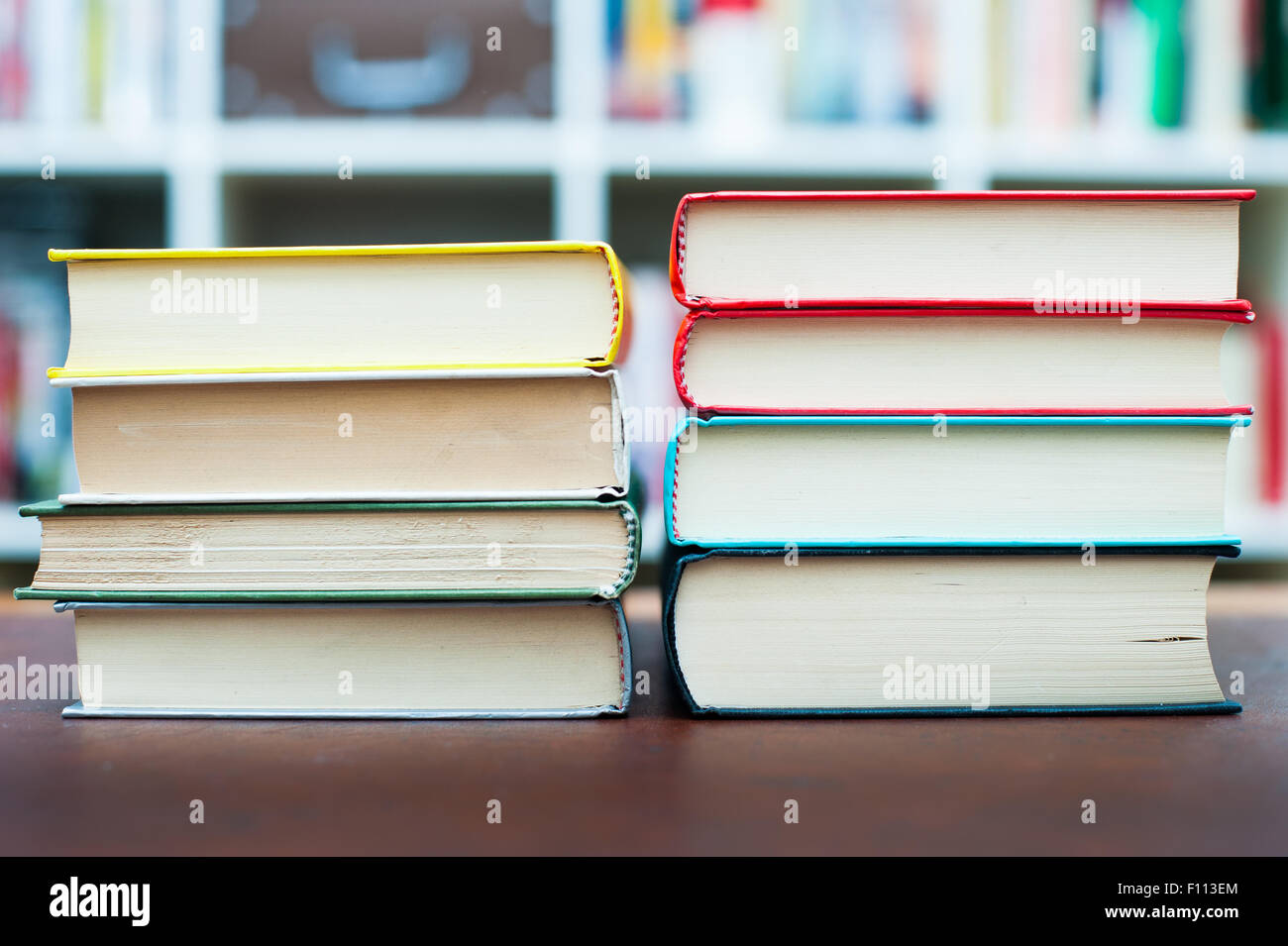 Two piles of different colors books on desktop with library in ...