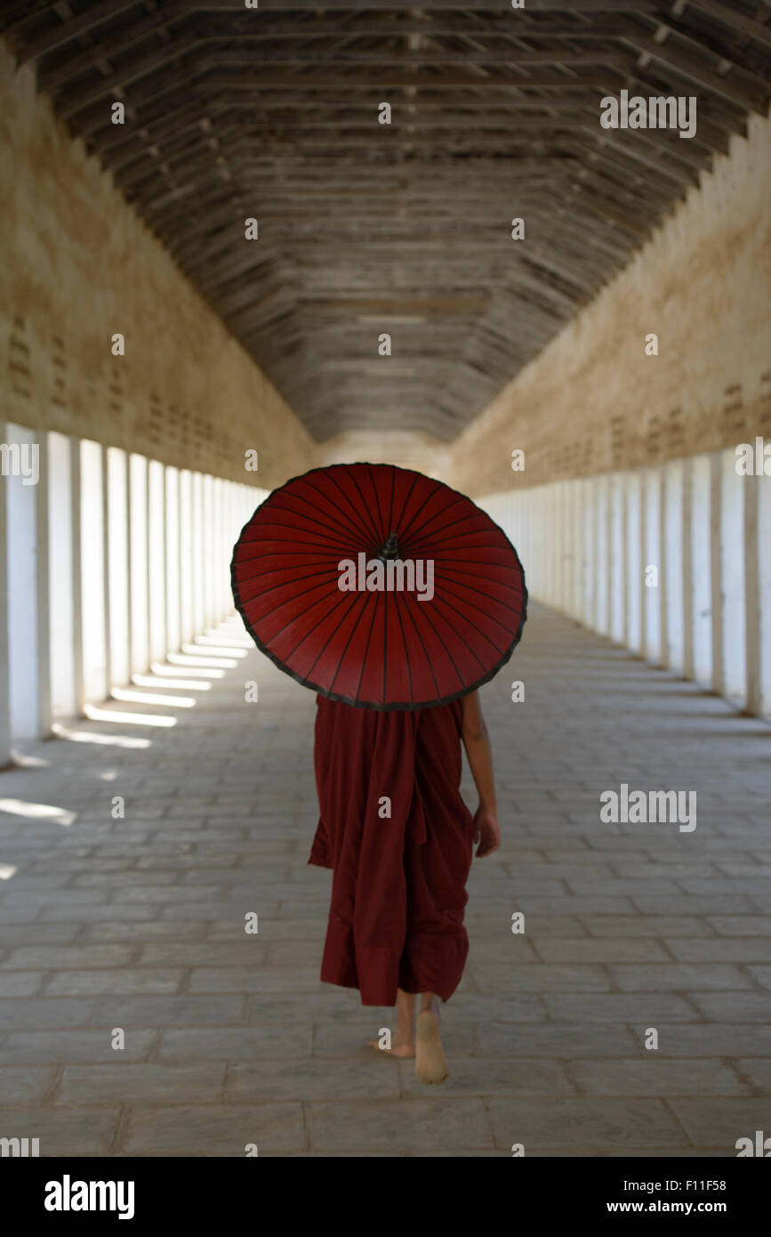 Asian monk-in-training carrying parasol in hallway Stock Photo