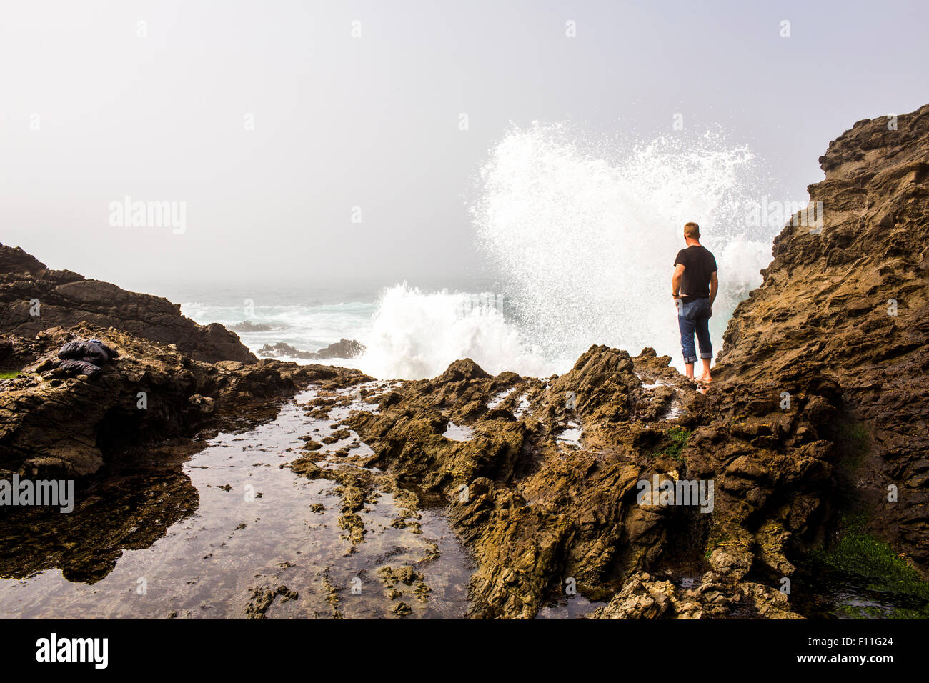 Caucasian hiker watching crashing ocean waves Stock Photo