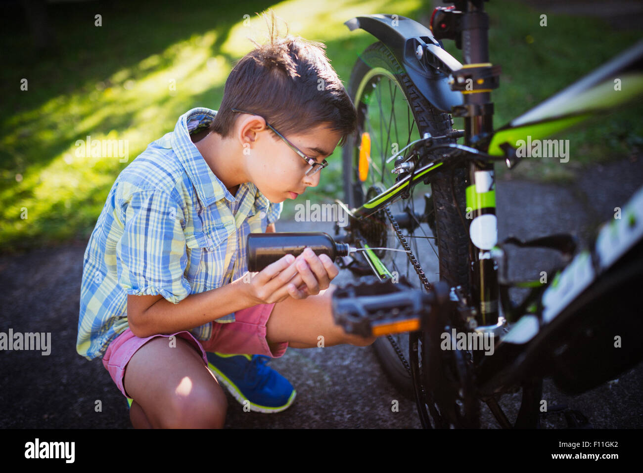 Mixed race boy oiling bicycle chain in backyard Stock Photo