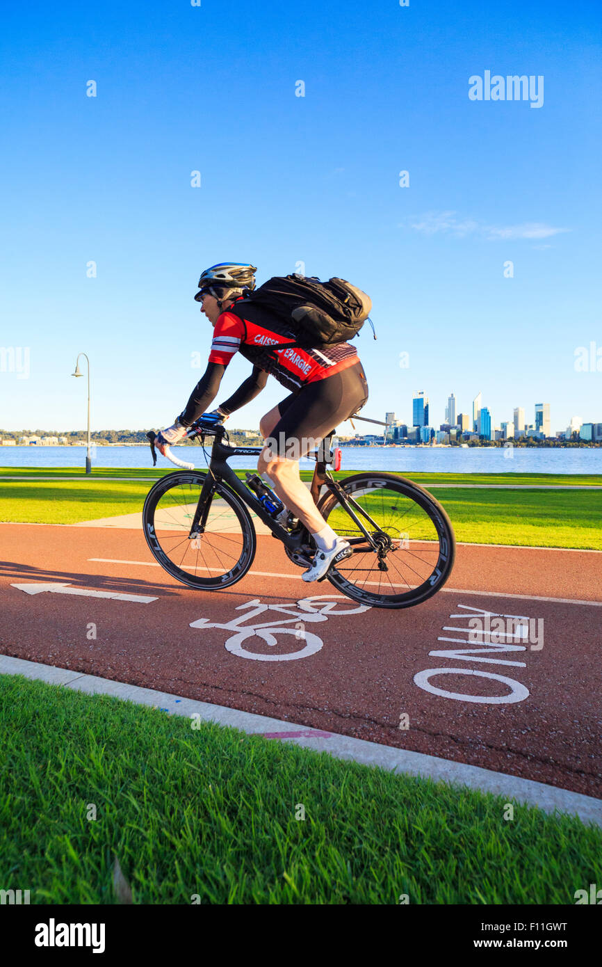 A male cyclist with a backpack riding down a bike only path with a city skyline in the distance Stock Photo