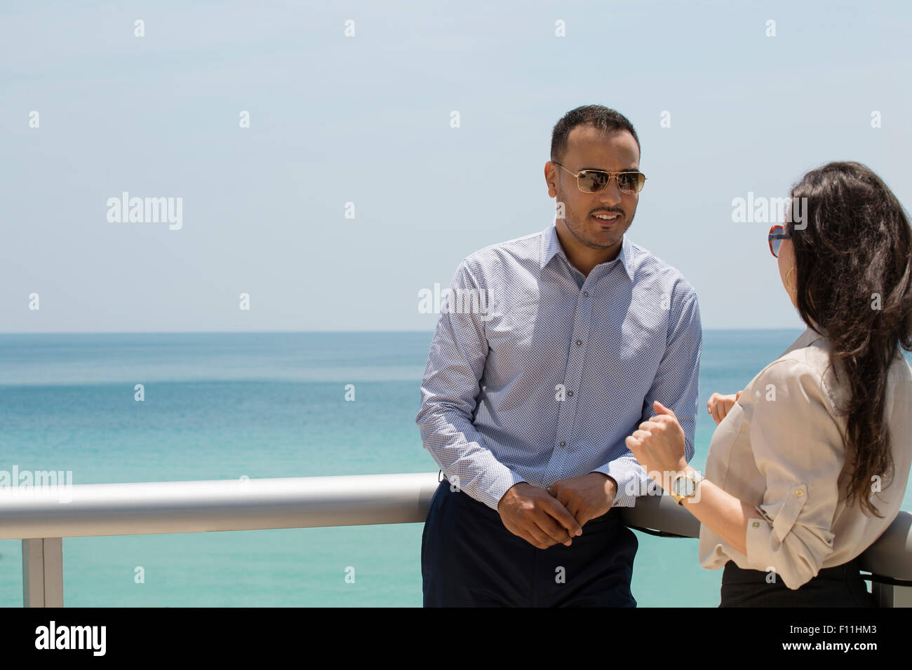Business people talking on balcony over ocean Stock Photo