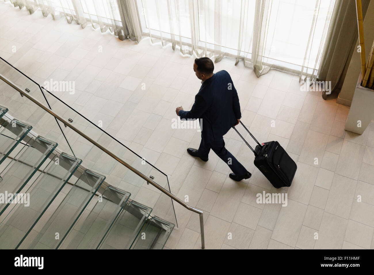 High angle view of Hispanic businessman rolling luggage in hotel lobby Stock Photo