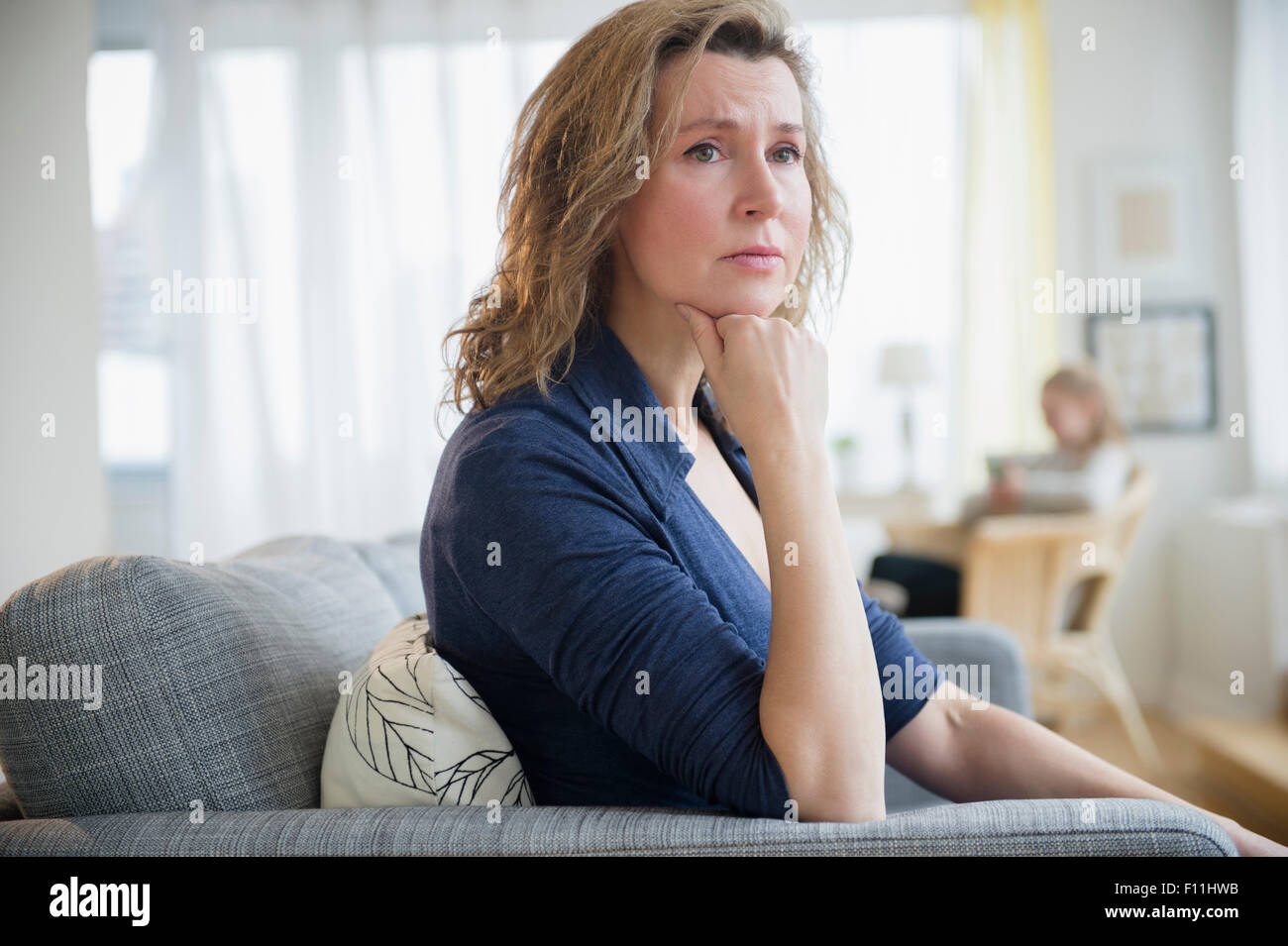 Concerned Caucasian woman sitting on sofa Stock Photo