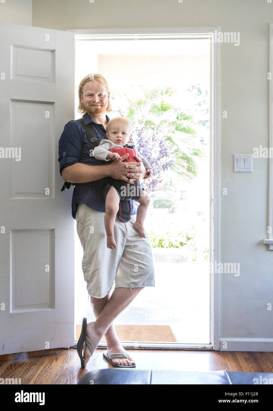 Caucasian father wearing son in harness in doorway Stock Photo