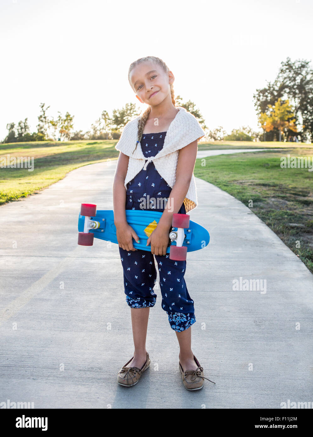 Mixed race girl holding skateboard in park Stock Photo
